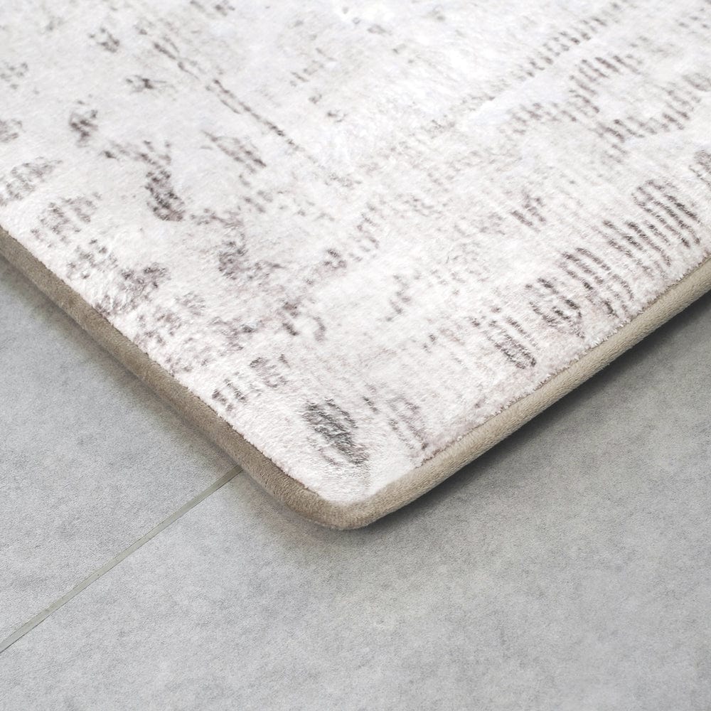 Close-up of a light-colored rug with faint patterns on a tiled floor.