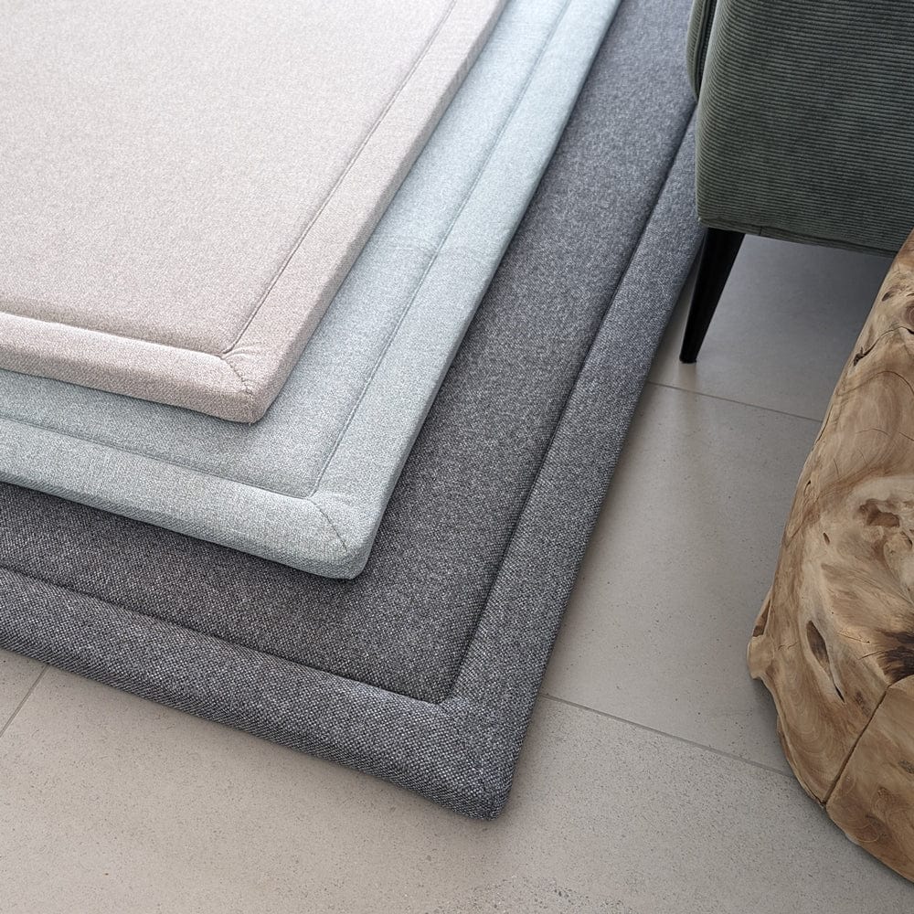 Stacked fabric mats in shades of grey and blue on a tiled floor.