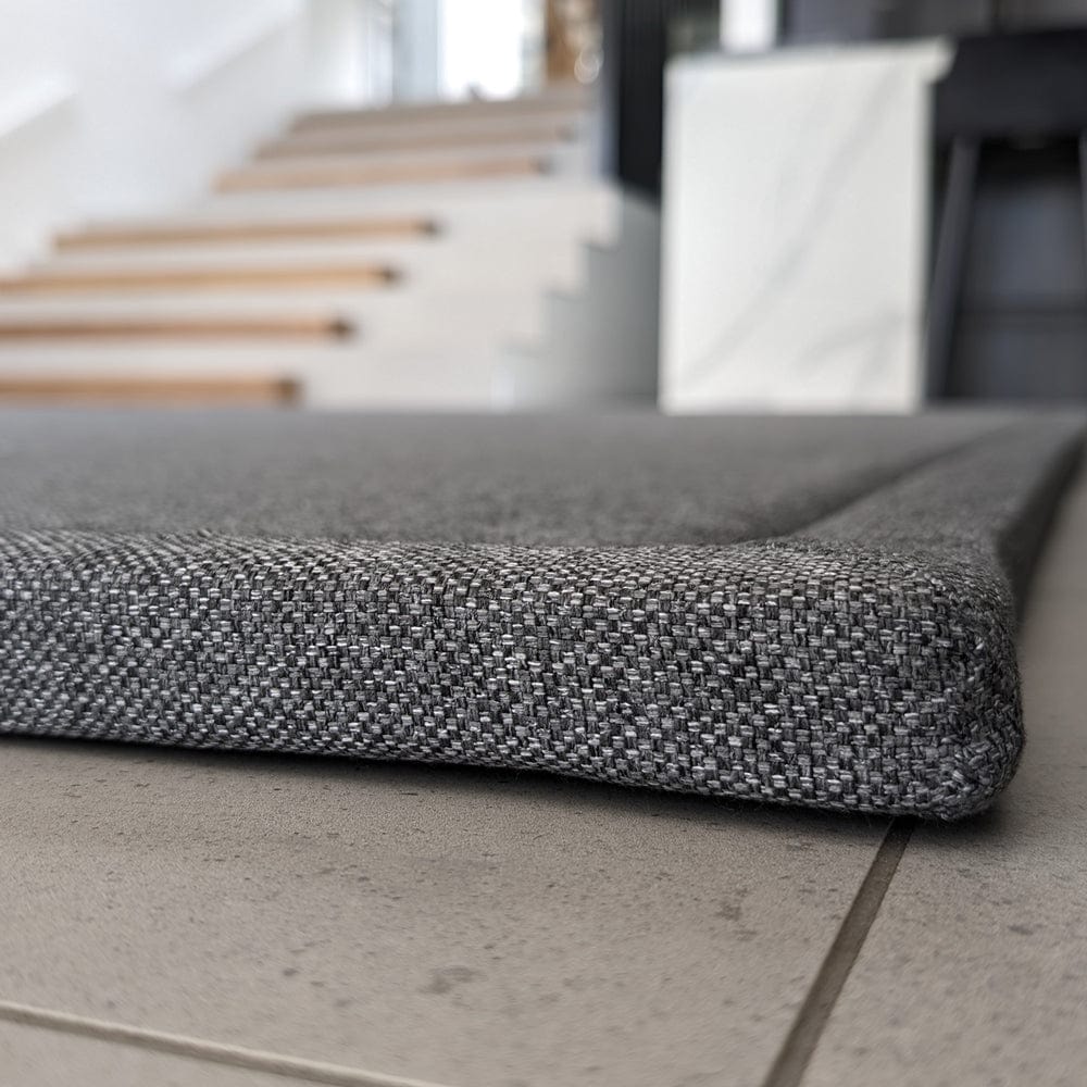 Close-up of a gray woven mat on a tiled floor with stairs in the background.